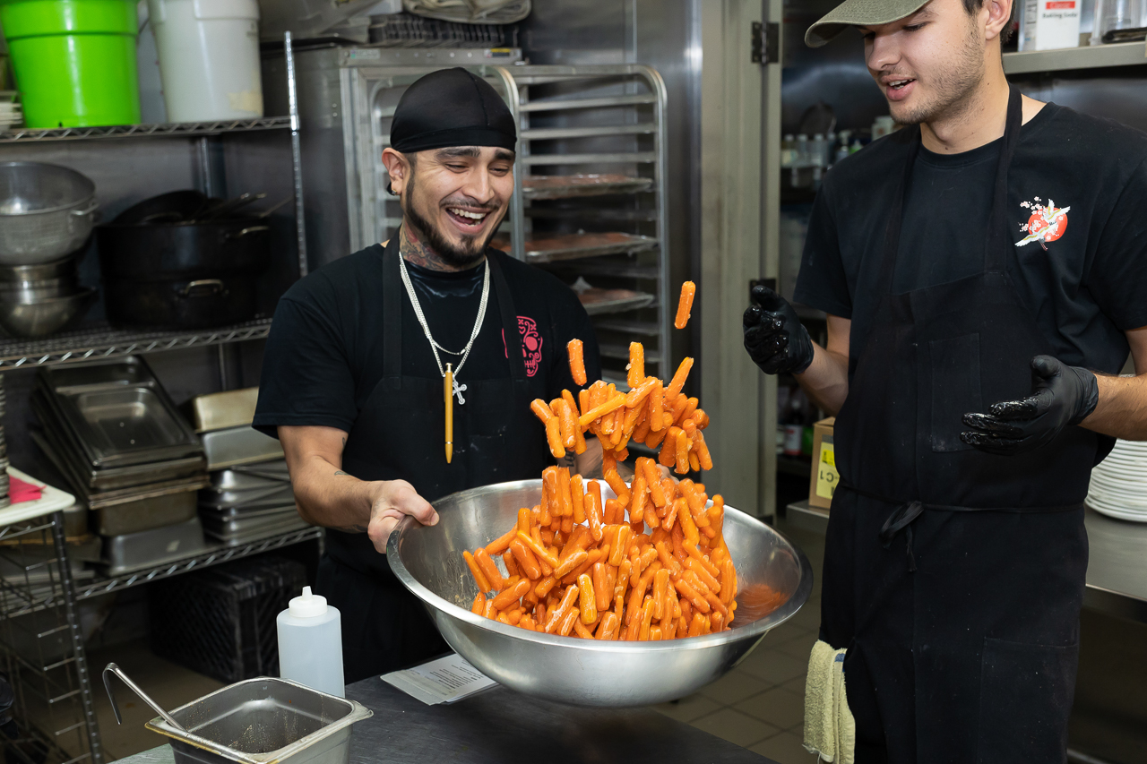 The chef tosses carrots while the apprentice chef looks on during the Primavera Foundation fundraiser, a seasonal event that pairs community members with chefs to put on a multiple course meal. The fund raised benefit the Primavera Foundation programs.